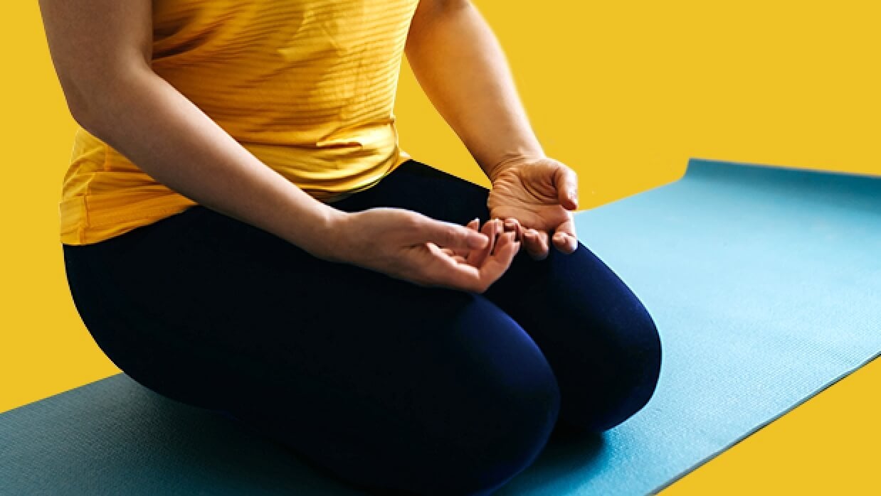 Persona arrodillada con las palmas de su mano hacia arriba sobre su falda en una estera de yoga.